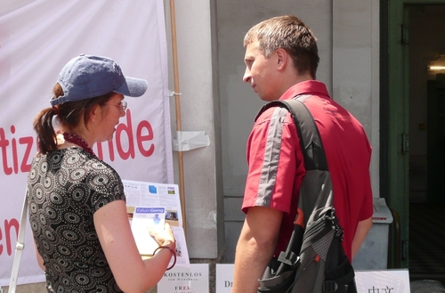Eine Falun Gong Praktizierende erklärt einem Passanten die aktuelle Verfolgung von Falun Gong in China und wie diese durch die kommunistische Partei auch ins Ausland übertragen wird.